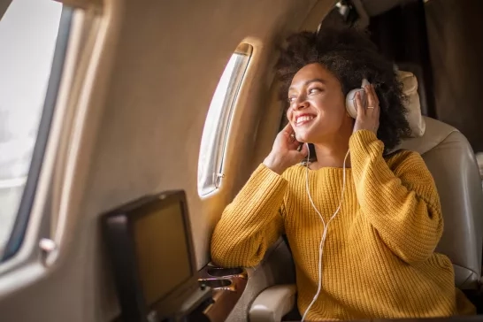 Young woman sitting on an airplane looking through the window listening to music