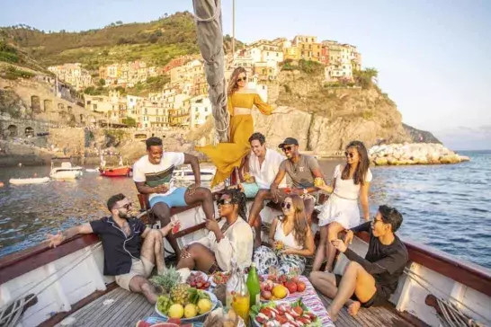 A group of travelers enjoy a lively day on a boat, sailing along the beautiful coastline of Cinque Terre, Italy.