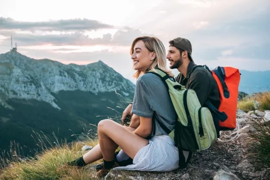 A young couple sitting aside a mountain smiling after their hike. 