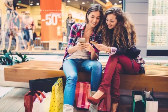 Two women sitting on shopping mall bench with shopping bags