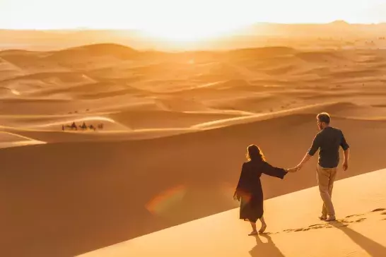 A couple holding hands in the sunset in the Sahara Desert.