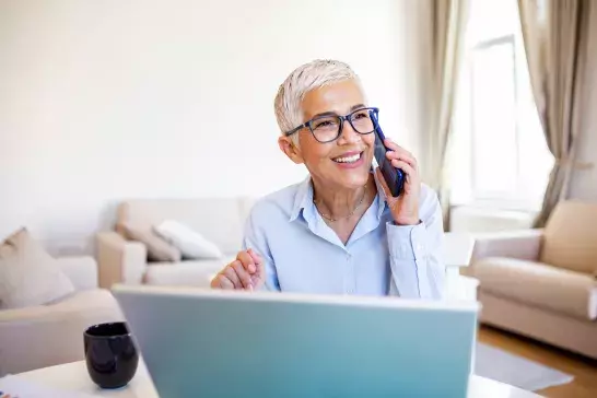 older woman talking on phone in front of laptop