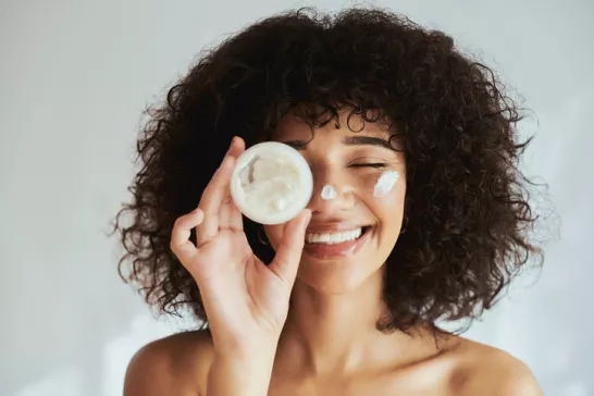 Woman holds jar of face cream while doing skin care routine