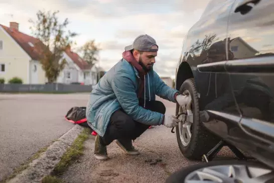 man bends down to inspect and repair vehicle tire