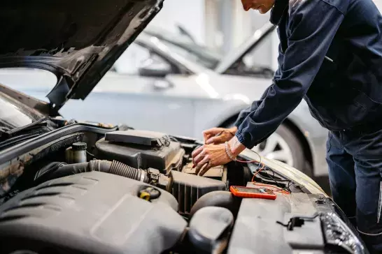 Young male car mechanic checking voltage on a car battery he is working on in his garage.