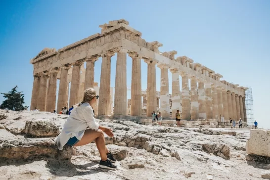 A woman sitting on a rock admiring the Parthenon Temple in Greece.