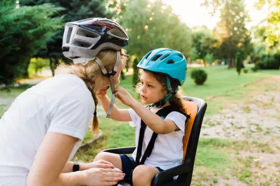 Young daughter buckling mother's bike helmet for protection