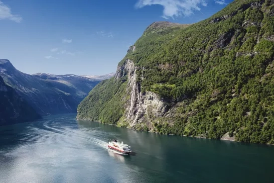 Hurtigruten's MS Nordly ship crossing through cliffsides in Norway.