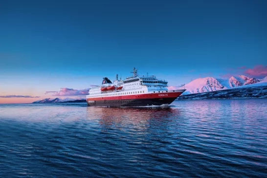 Hurtigruten Expeditions' MS Nordlys ship cruising through Norway at sunset.