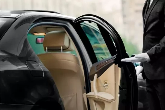 A person in white gloves holding the door open of a luxury car.