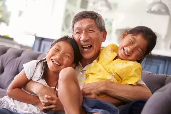 Grandfather hugging grandson and granddaughter on living room couch