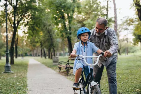 Grandfather teaching boy how to ride a bike on a sunny day in the park