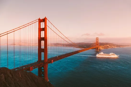 Beautiful panorama view of cruise ship passing famous Golden Gate Bridge with the skyline of San Francisco in the background in beautiful golden evening light at sunset in summer, California, USA