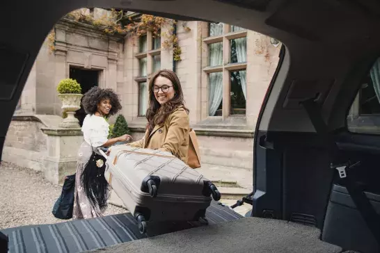 Two friends arrive at a hotel where they are unloading their suitcases from their car trunk