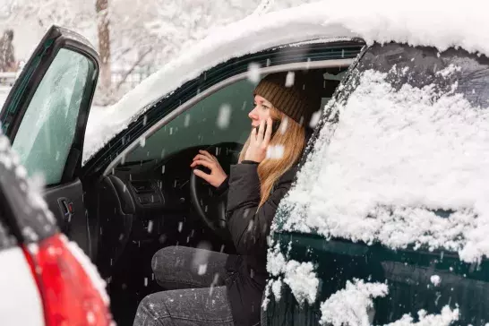 woman calling for assistance inside snow covered car