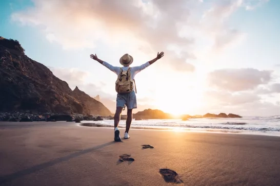 Solo traveller stretching his arms by the sea at sunrise.