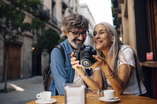 Portrait of a mature couple on vacation enjoying at the sidewalk cafe in Barcelona and watching photos on their camera.