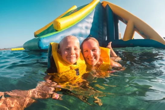 Mother and child wearing lifejackets in water at waterpark