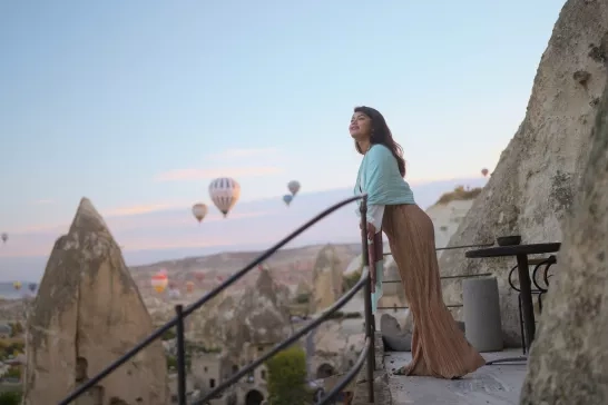 Portrait of young female tourist watching hot air balloons from balcony in Cappadocia during her travel.