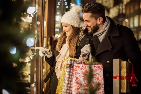svetikd | iStock Young couple walking in downtown for Christmas. Holding Christmas gifts and big Teddy bear. Wearing warm clothing.