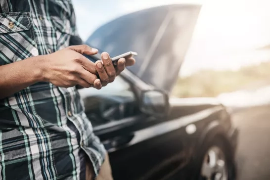 man-looking-at-cell-phone-by-broken-down-car