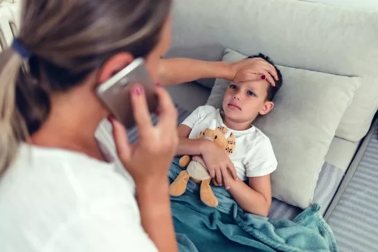 Mother checking sick child's temperature while calling doctor