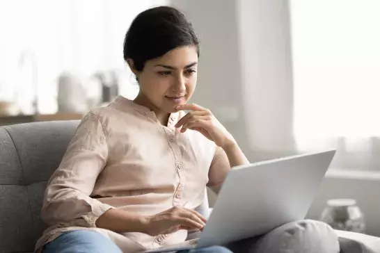 Pensive woman reviewing digital document on laptop while sitting on couch