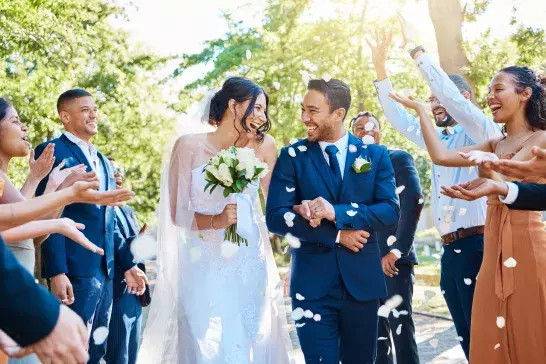 Wedding guests throwing rose petals confetti tradition over bride and groom