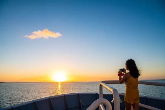 A child taking a photo off the National Geographic LIndblad Expeditions ship at sunset