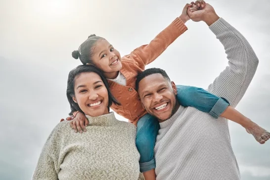 Kid sitting on father's shoulders, and leaning on mom