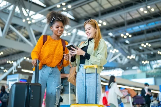 Two woman friends with luggage walking together at airport terminal