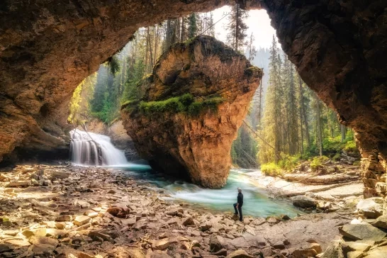Man Standing In Cave Against Waterfall At Forest