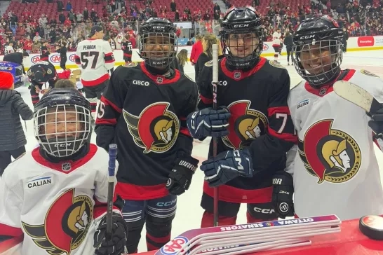 Four youth hockey players, wearing Ottawa Senators gear, posing at bench.