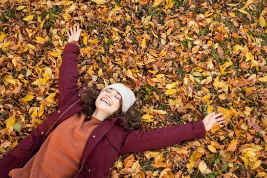 woman lying over autumn leaves with stretched arms 