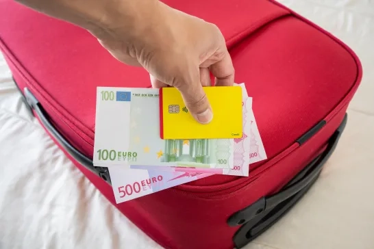 Euros and yellow credit card on a red suitcase on a bed