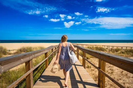 woman tourist walking from beautiful sunny sandy beach Meia Praia on wooden promenade. Vacation in Lagos, Algarve, Portugal.