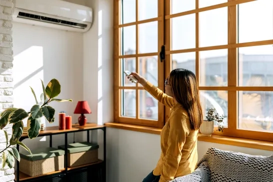 woman sitting on the couch and using the remote to change the room temperature of the ac unit 