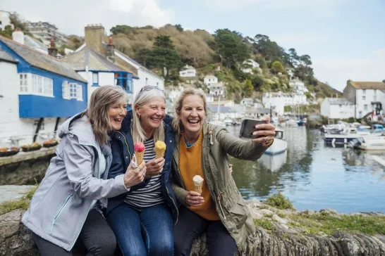 Female friends sitting on a wall and taking a selfie together on a mobile phone while eating an ice cream 
