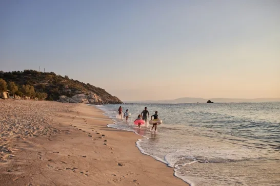 Family running and playing in the shallow water at the beach during summer sunset