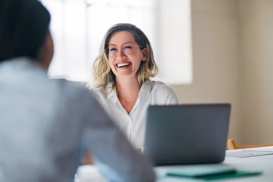 A cheerful woman with glasses is sitting at a desk