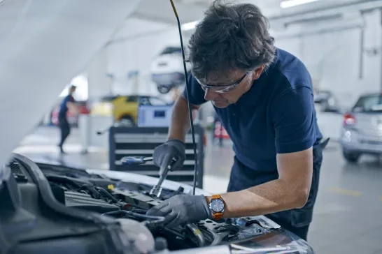 Male Mechanic With Socket Wrench Working On Car Engine In Auto Repair Shop