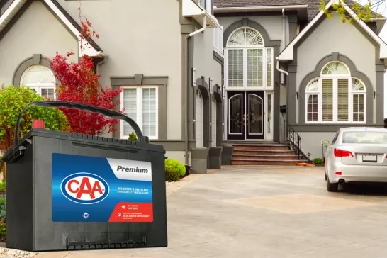 CAA Premium battery in front of a house with a car parked in the driveway.
