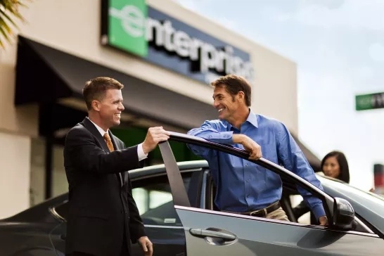 A couple of men smiling beside a car, outside an Enterprise rental office