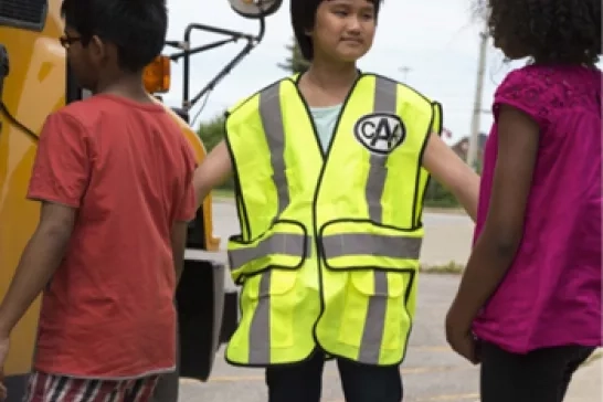 a child wearing a CAA vest helping kids onto a school bus