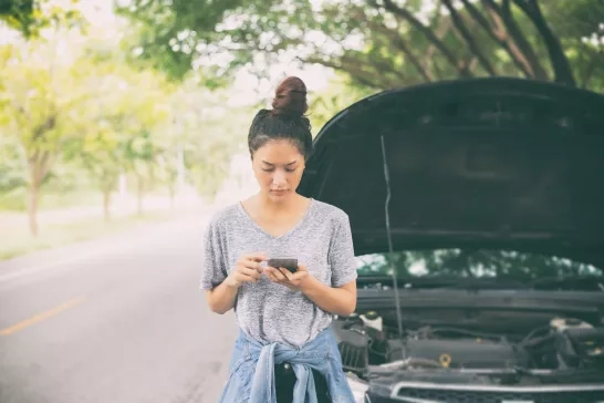 Asian woman using mobile phone to request roadside assistance