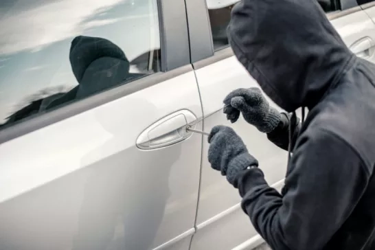 A hooded thief picking the lock of a car