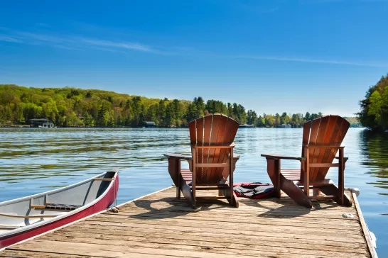 Dock with 2 adirondack chairs on it with a canoe in the lake