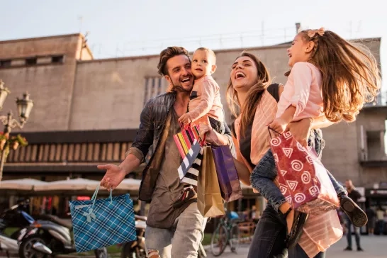 Young cheerful parents having fun with their children during shopping day in the city.