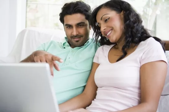 A couple sitting on a couch looking at a laptop