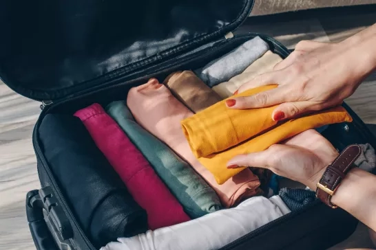 Top view of tourist woman open suitcase for pack and arranging colorful cloths for travelling.